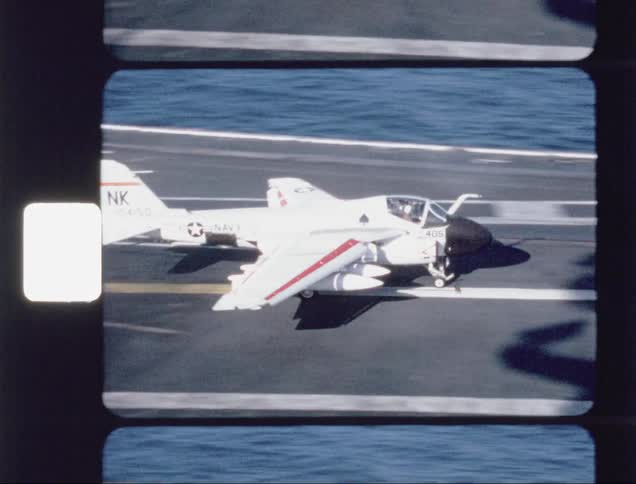 People photograph a jet landing on an aircraft carrier at sea