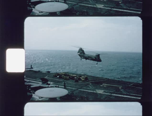 A helicopter is delivering cargo to an aircraft carrier during the day