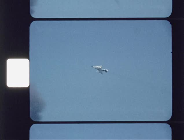 A fighter jet is flying over the ocean as people look on during the day