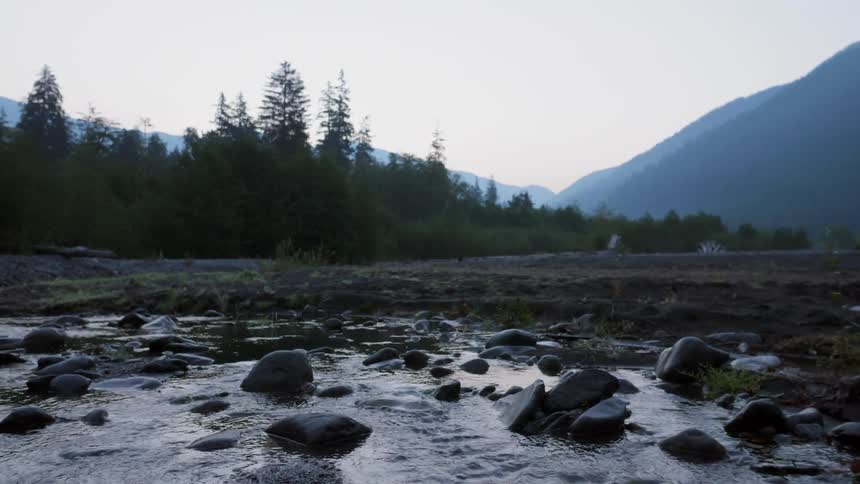Water in a river is trickling over rocks in a mountain valley at dawn