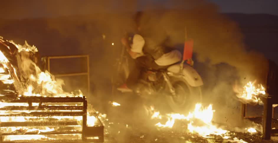 Man rides a motorcycle through a burning building