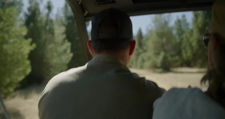 A man rides in a vehicle and points out towards the trees