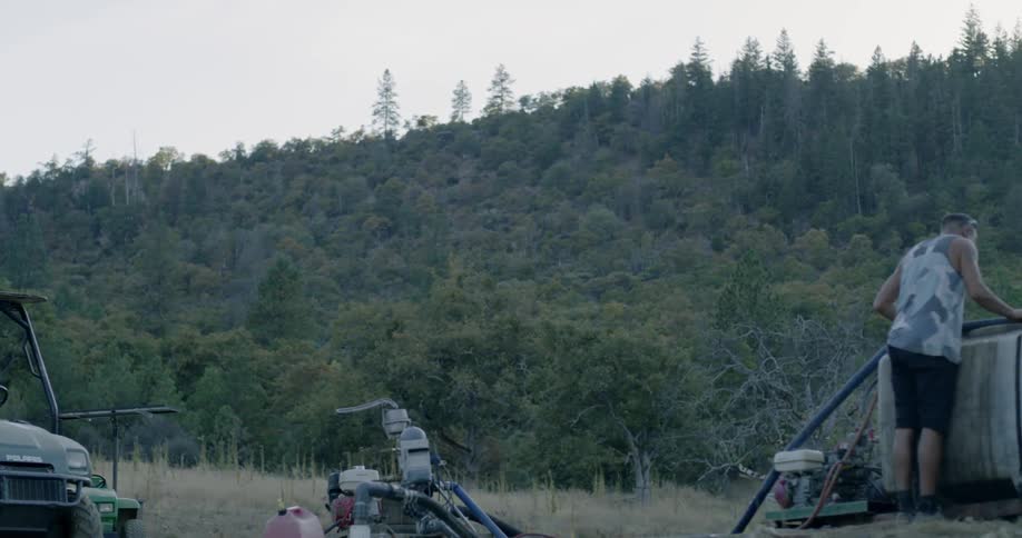 A man standing near an atv uses a pump to fill an outdoor tank