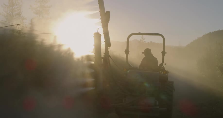 Farmer on a tractor sprays orchard with his sprayer
