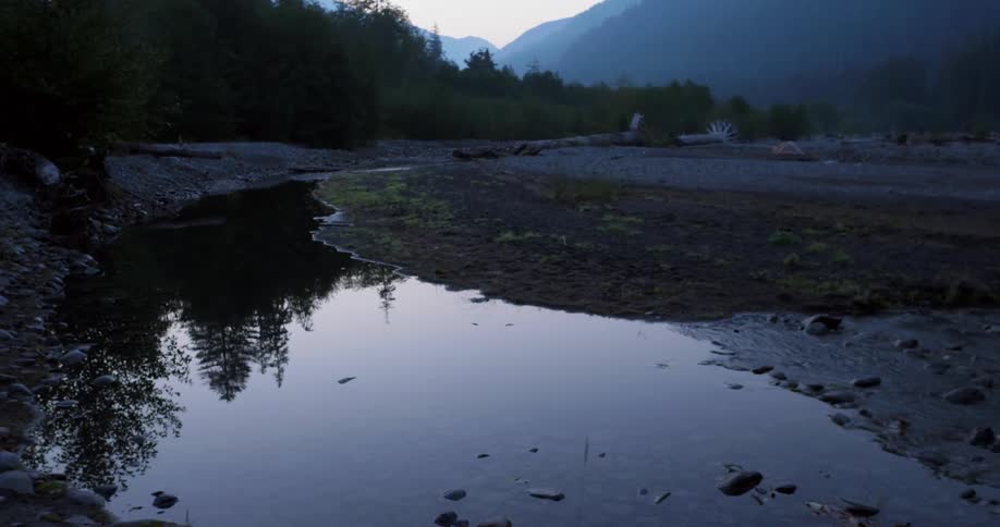 Water in a riverbed is reflecting its natural setting at dawn
