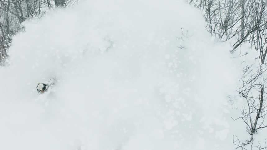 A skier is turning through deep snow as he goes down a hillside in daylight