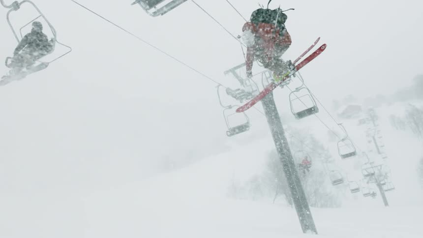 Skiers ride on ski lifts as another skier performs a jump