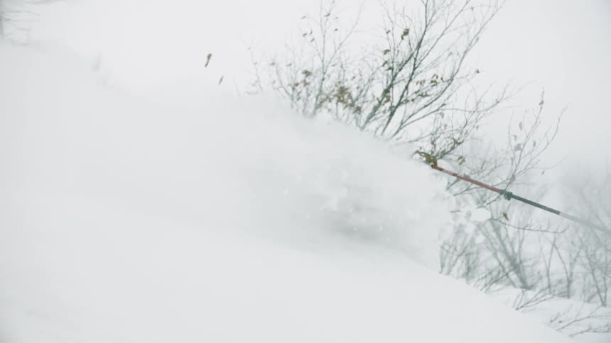 A skier is kicking up deep powder as he skis downhill during the day