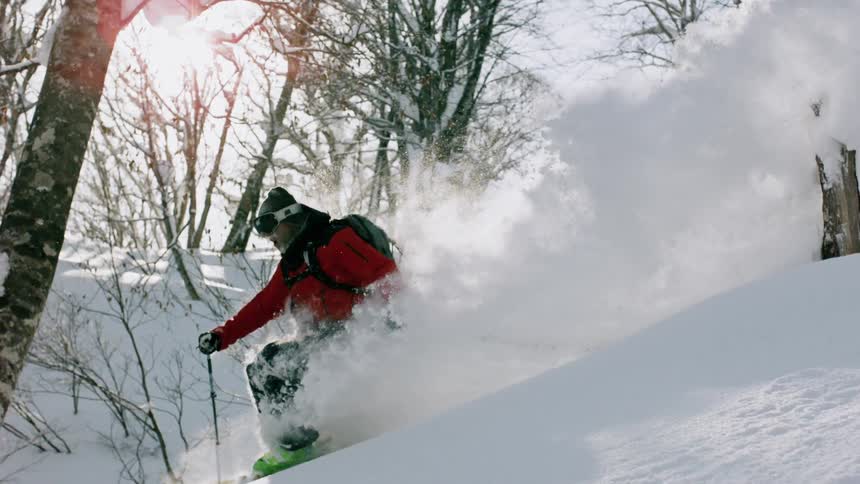 A skier is kicking up a plume of snow as he skis downhill during the day