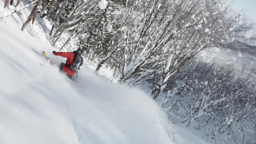 A skier turns through deep snow as he goes down a hillside in daylight