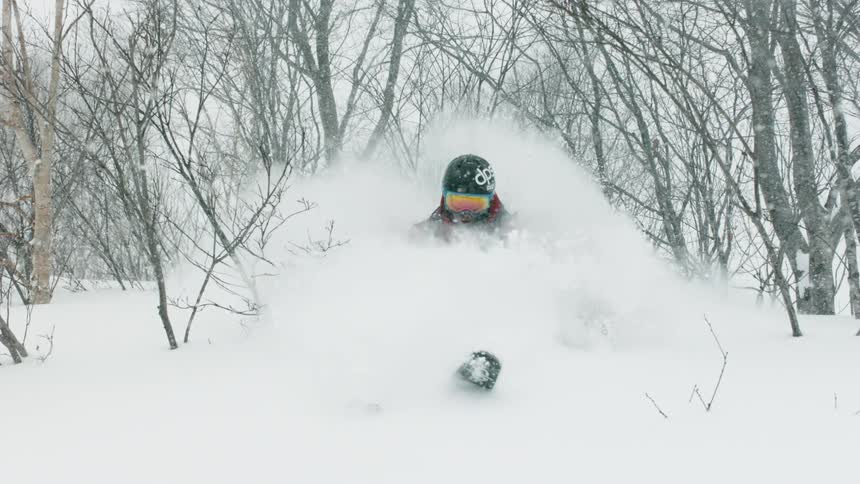 A skier is turning through deep snow as he goes down a hillside in daylight