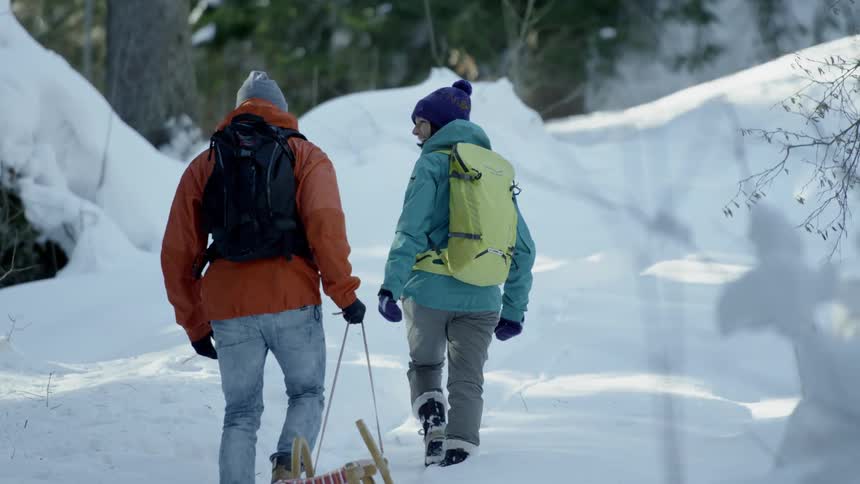 Two people hold hands as they drag a sled through the snow