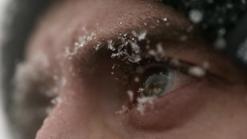 A snowflake bounces off a man's eye in slow motion