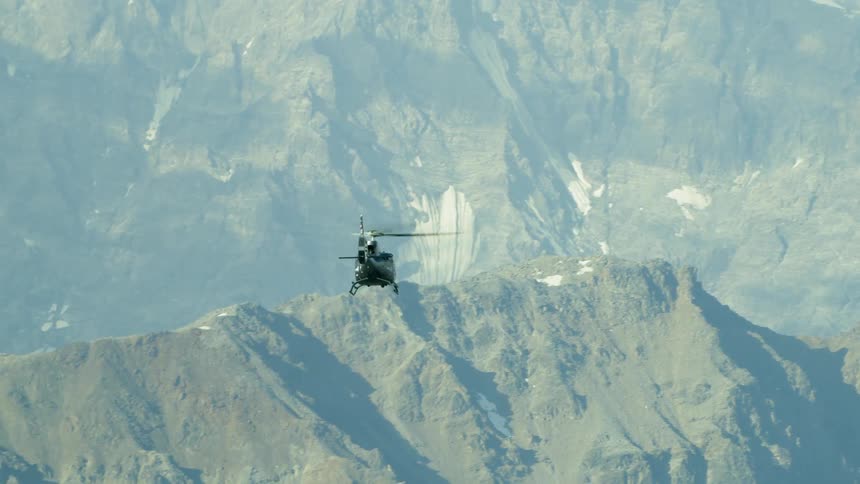 A helicopter moves high above the mountain