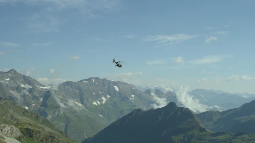 A helicopter turns and flies over rocky peaks