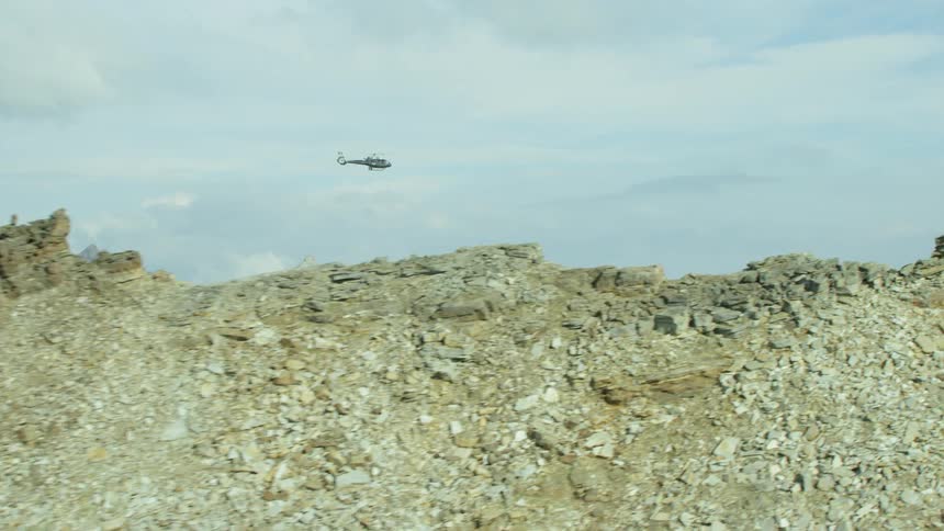A helicopter flies over some mountains on a cloudy day