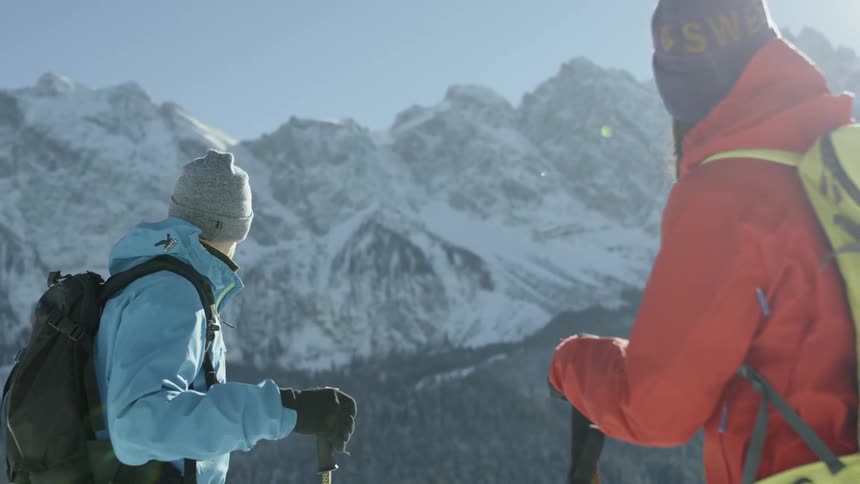 Two skiers are standing and looking at a mountain range during the day
