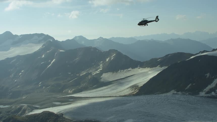 A helicopter is flying above a mountain range in daylight