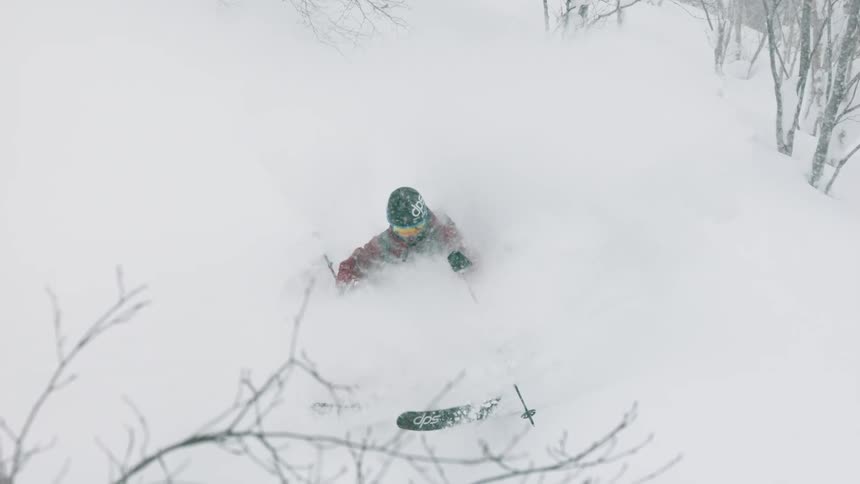Person skiing down a mountainside in deep snow on a cloudy day