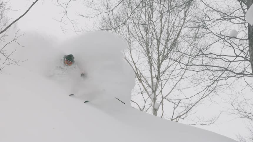A skier is turning through deep snow as he goes down a hillside in daylight