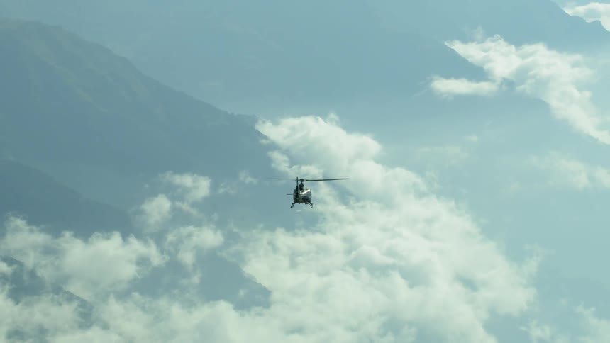 A helicopter flies over clouds and mountains