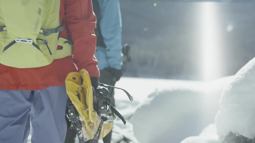 Two people are carrying snowshoes and ski poles as they hike on a winter day
