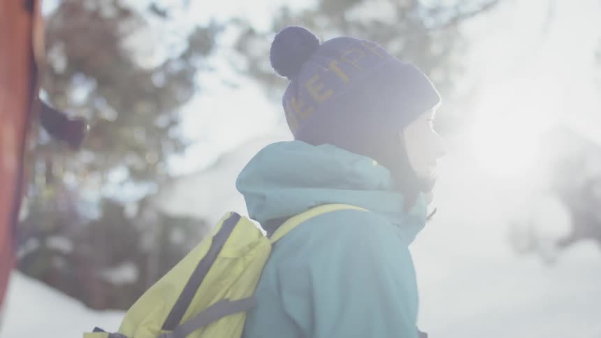 A woman backpacking in the snow looks back and smiles at her companion