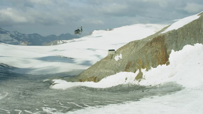 A helicopter is flying past a chalet in the mountains during the day