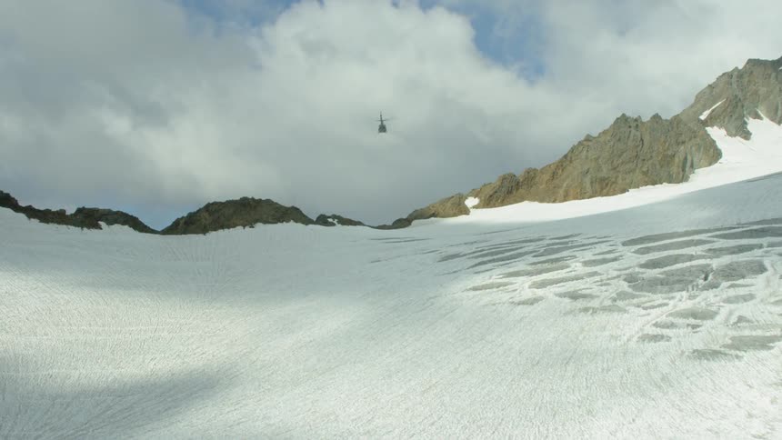 A helicopter flies above a snow covered mountain