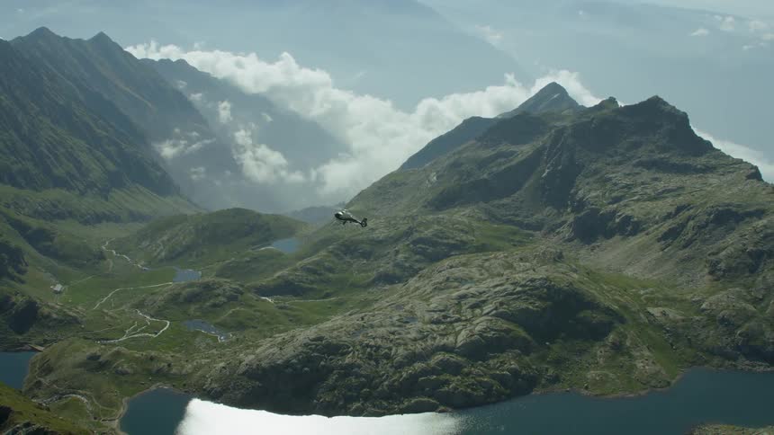 A helicopter flies above a lake between tall mountains