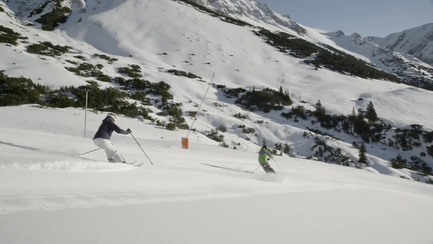 Two skiers are skiing down a mountain slope during the day