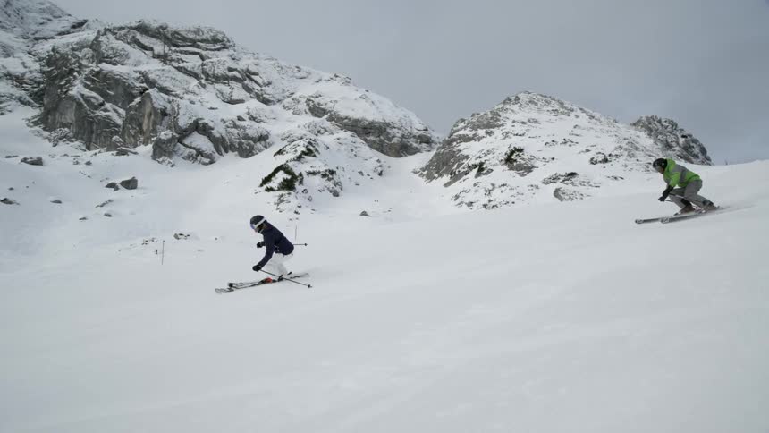 Two people ski down a snowy mountain