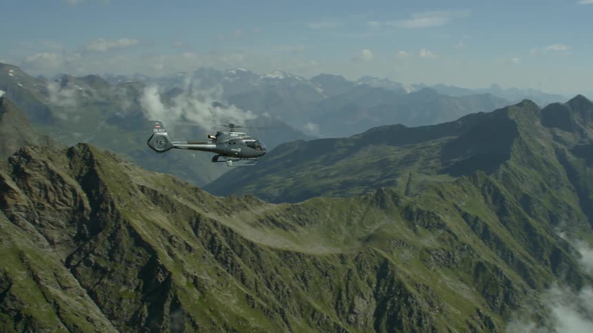 The helicopter moves high in the air above the cloud covered green mountains