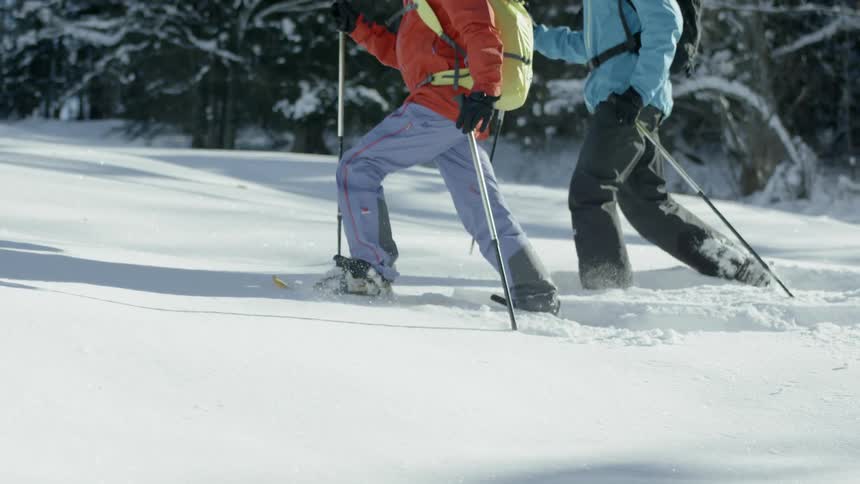 Two people are snowshoeing up a slope during the day
