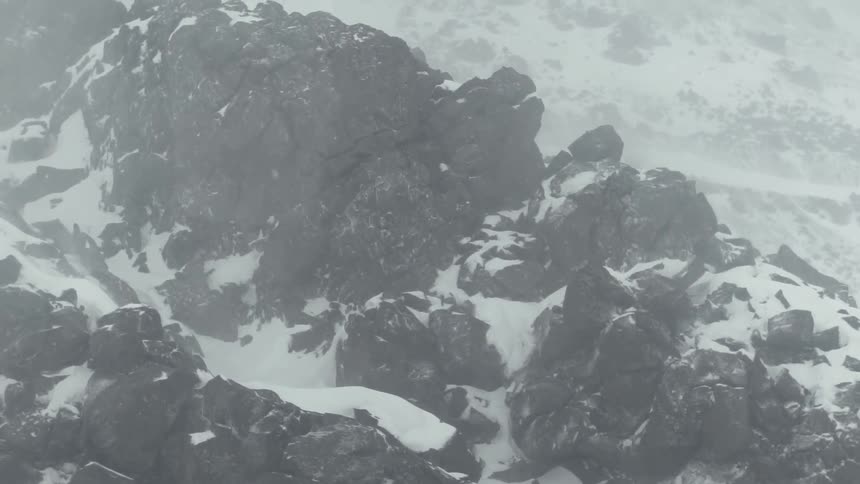 Snow falls on the top of a stone mountain