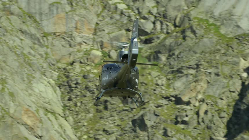 A helicopter is flying above a mountain cliffside in daylight
