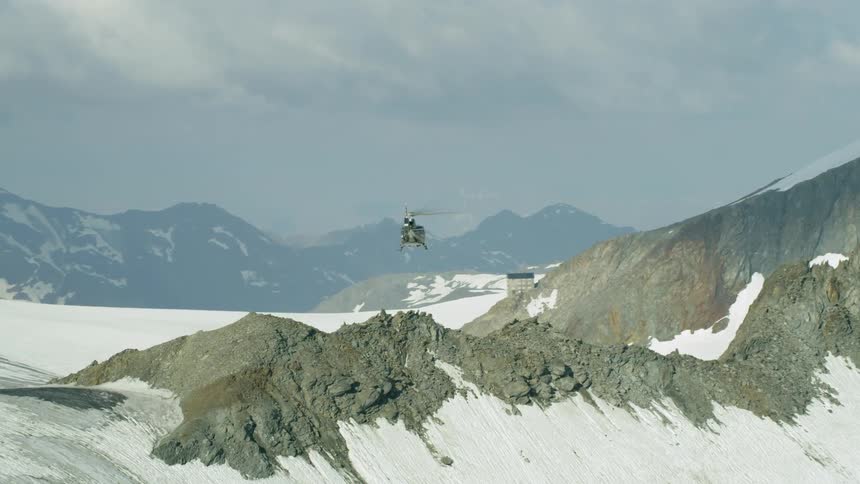 A helicopter is piloted over snowy mountains