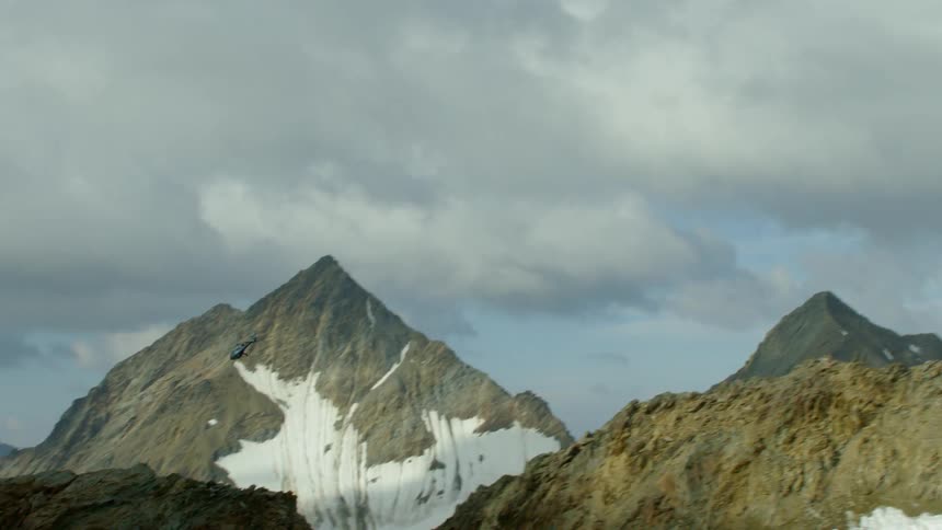 A helicopter is flying above a mountain range in daylight