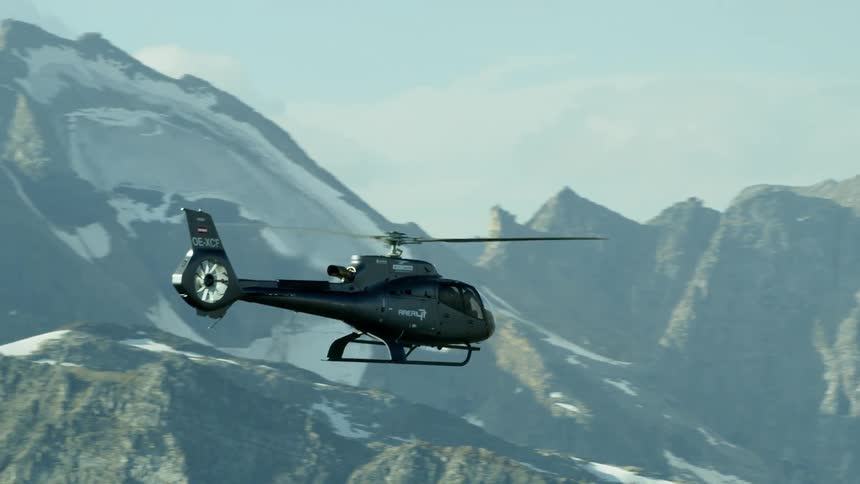 A helicopter is piloted over snowy mountains