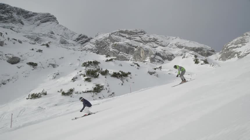 Two people ski down a mountain slope on a sunny day