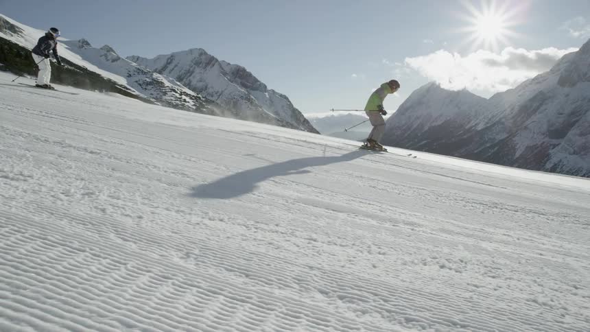 Two people ski together down the slope on a sunny day
