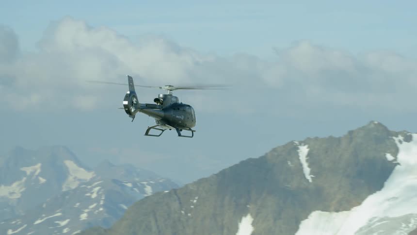 The black helicopter slowly moves in the air above the mountains