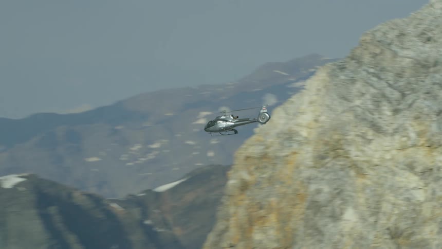 A helicopter is flying above a mountain range in daylight