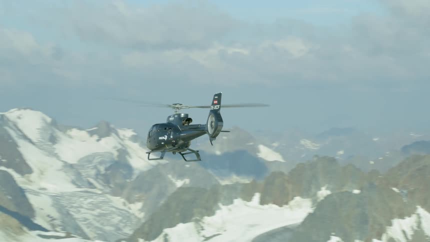 A helicopter is flying above a mountain range in daylight