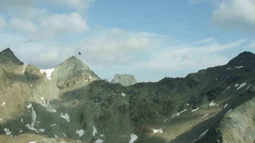 The helicopter moves past the mountain peaks
