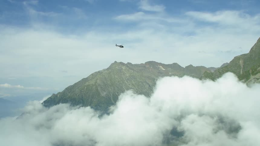 A helicopter is flying over mountain peaks above clouds during the day