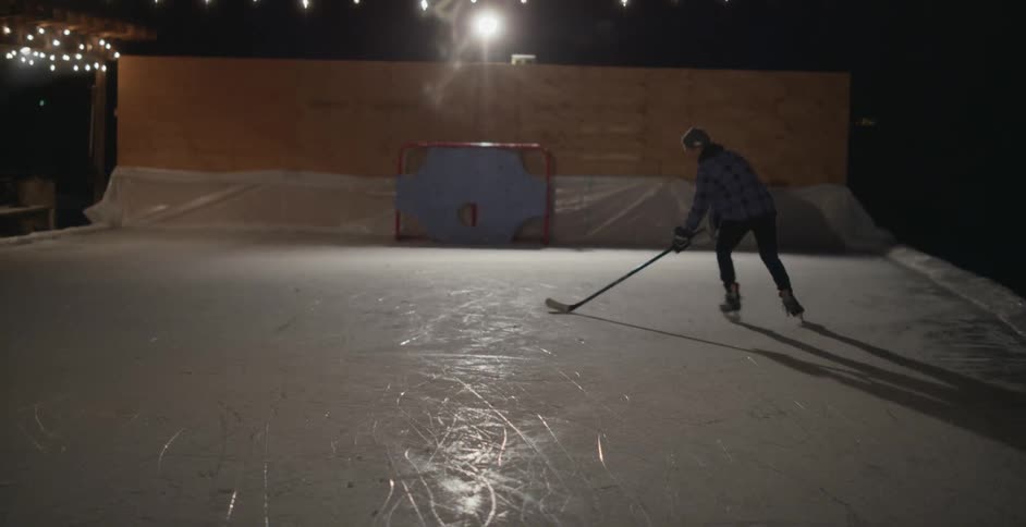 A man practices hockey on a rink outside at night