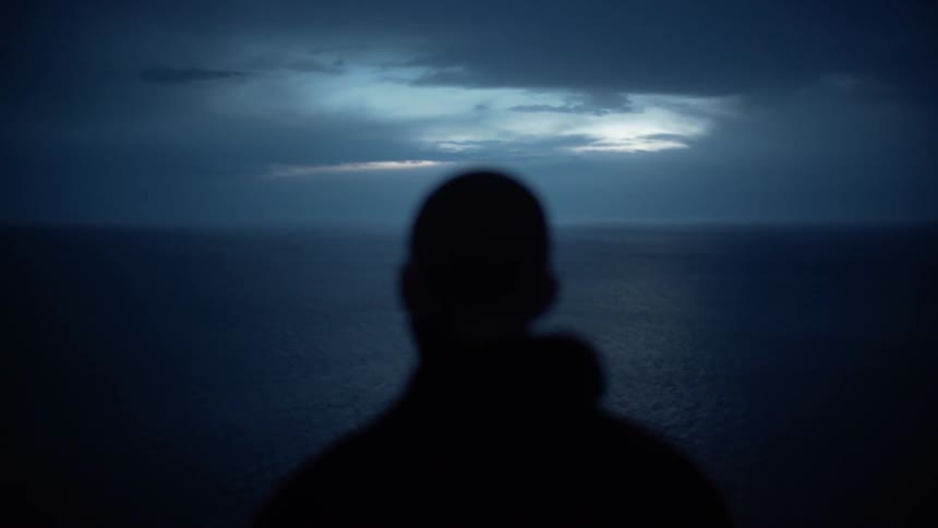 A man looks out onto the water with heavy clouds overhead