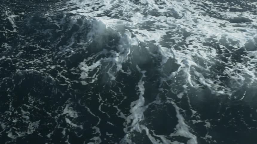 Rolling waves are creating foam trails on the ocean during the day
