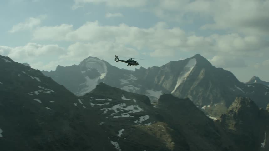 A helicopter flies above mountains